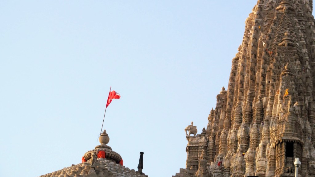 The towering flag and limestone structure of the Dwarkadhish temple by the sea.
