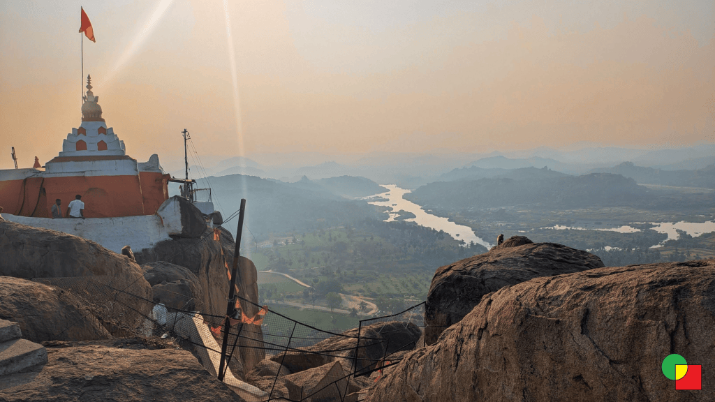 View from the top of Anjanadri Hill in Hampi, looking across a series of rugged hills and the Tungabhadra River winding through the landscape.
