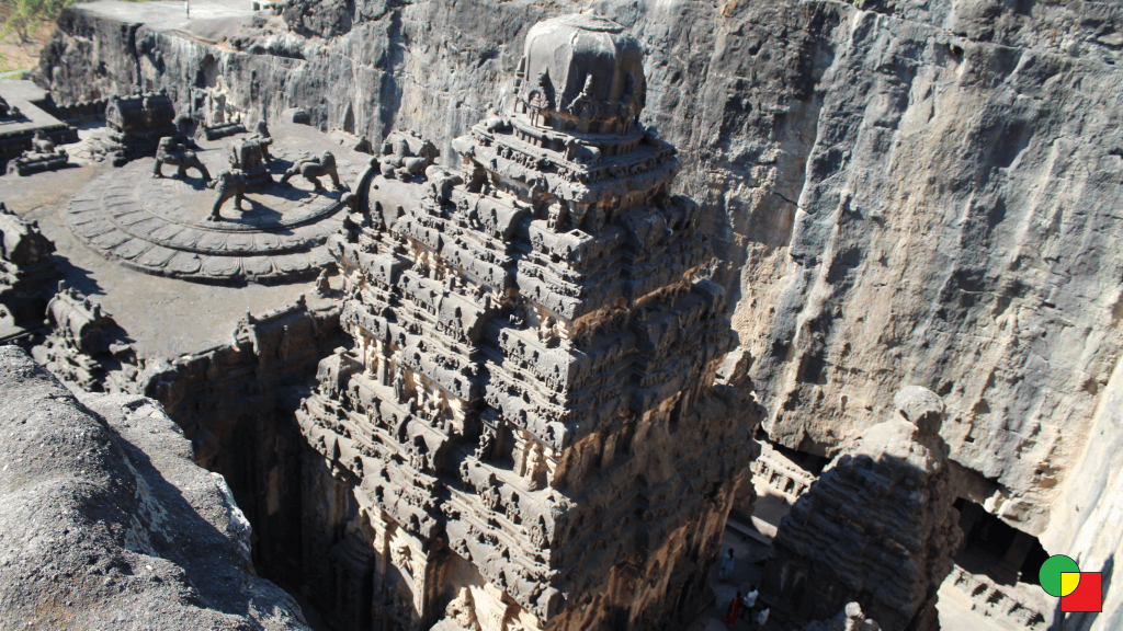 The Kailasa temple at Ellora, a multi-storey stone temple carved out of a basalt hillside, with cliff walls rising around it.